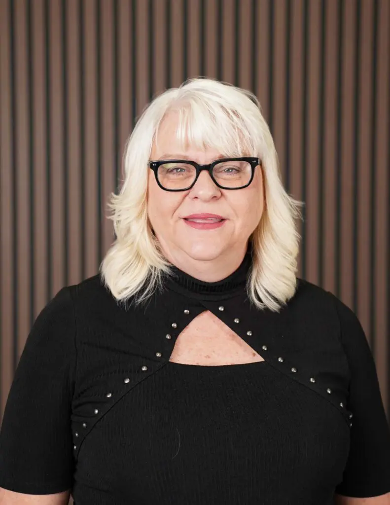 Woman with glasses and blonde hair smiling.