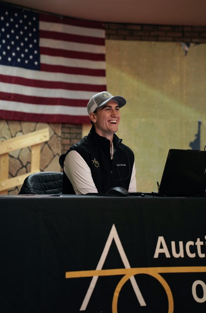 Man smiling beside American flag, sitting at desk.