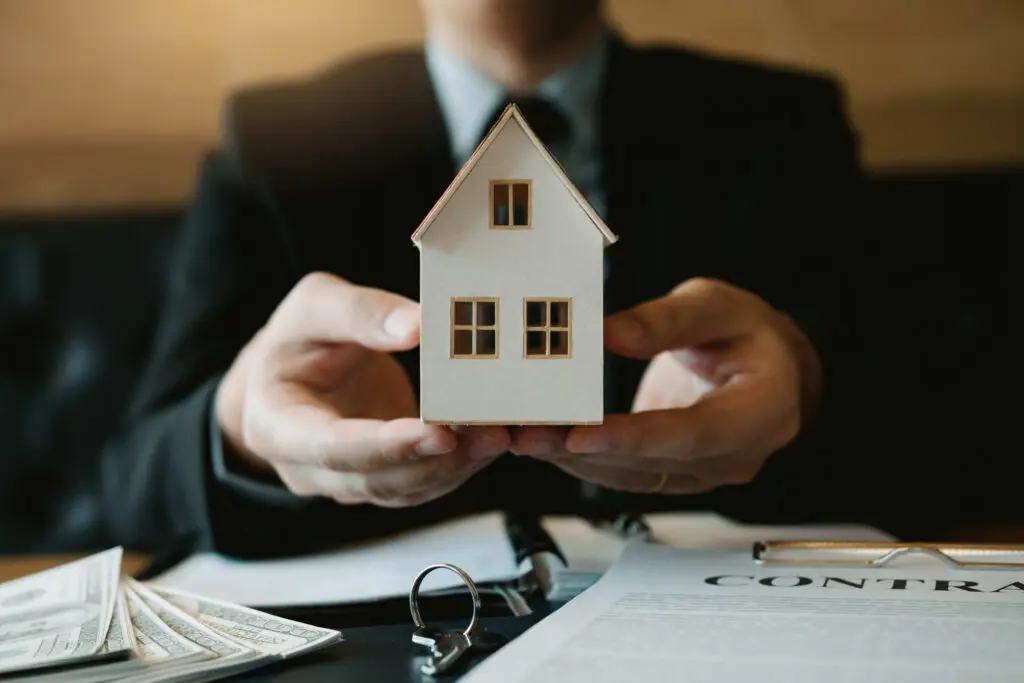 Businessperson holding model house over contract and money